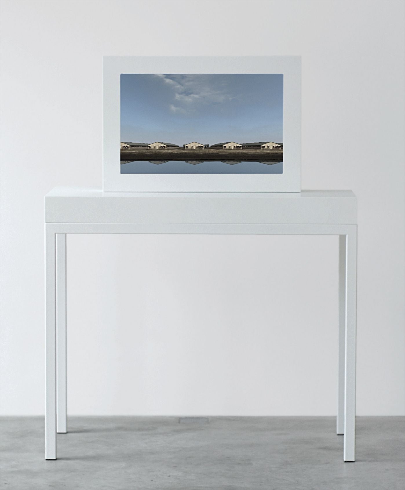 A white framed screen on a white table showing a row of long low farm sheds under a blue sky
