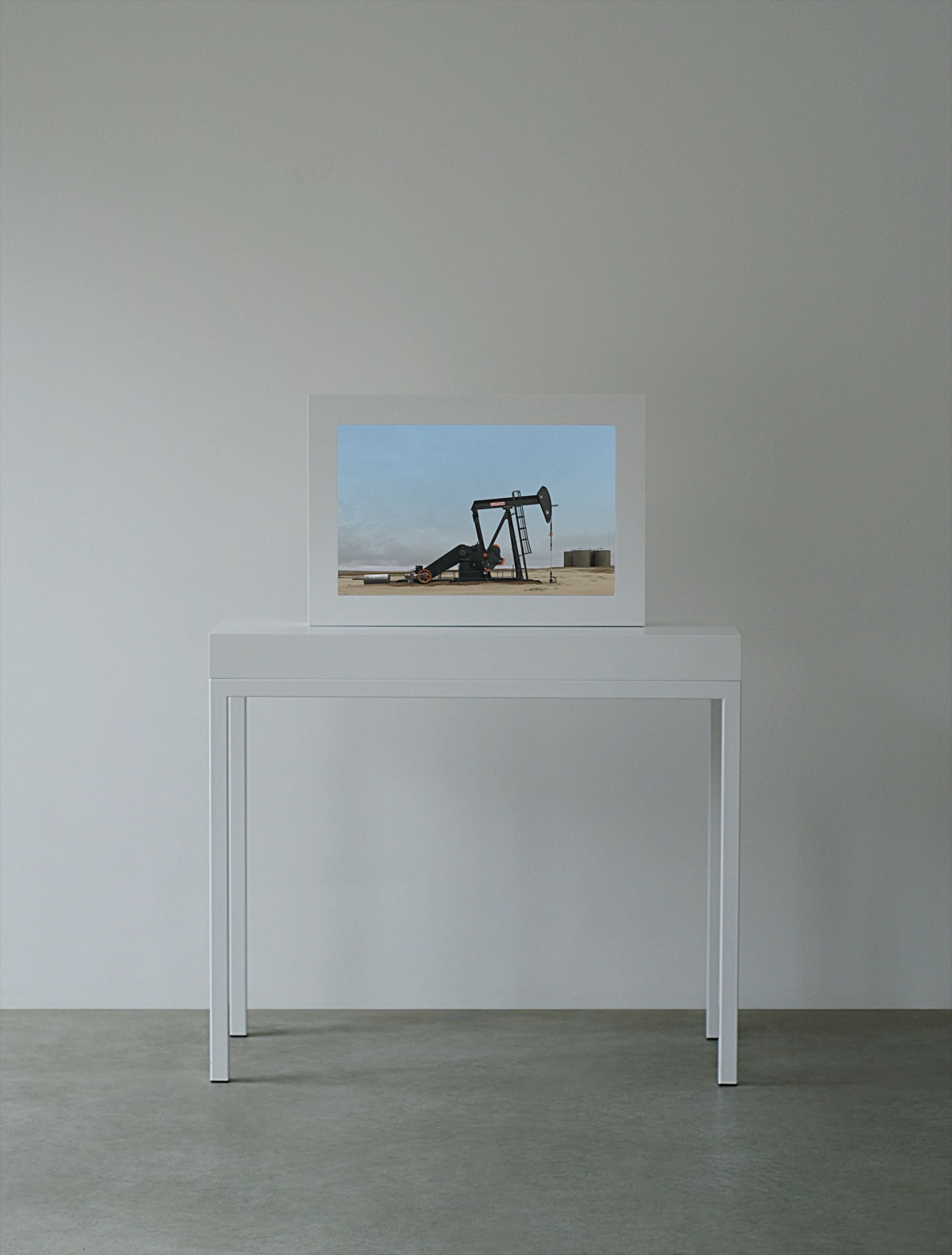 A white framed screen on a white table showing an oil pump jack in a flat brown desert