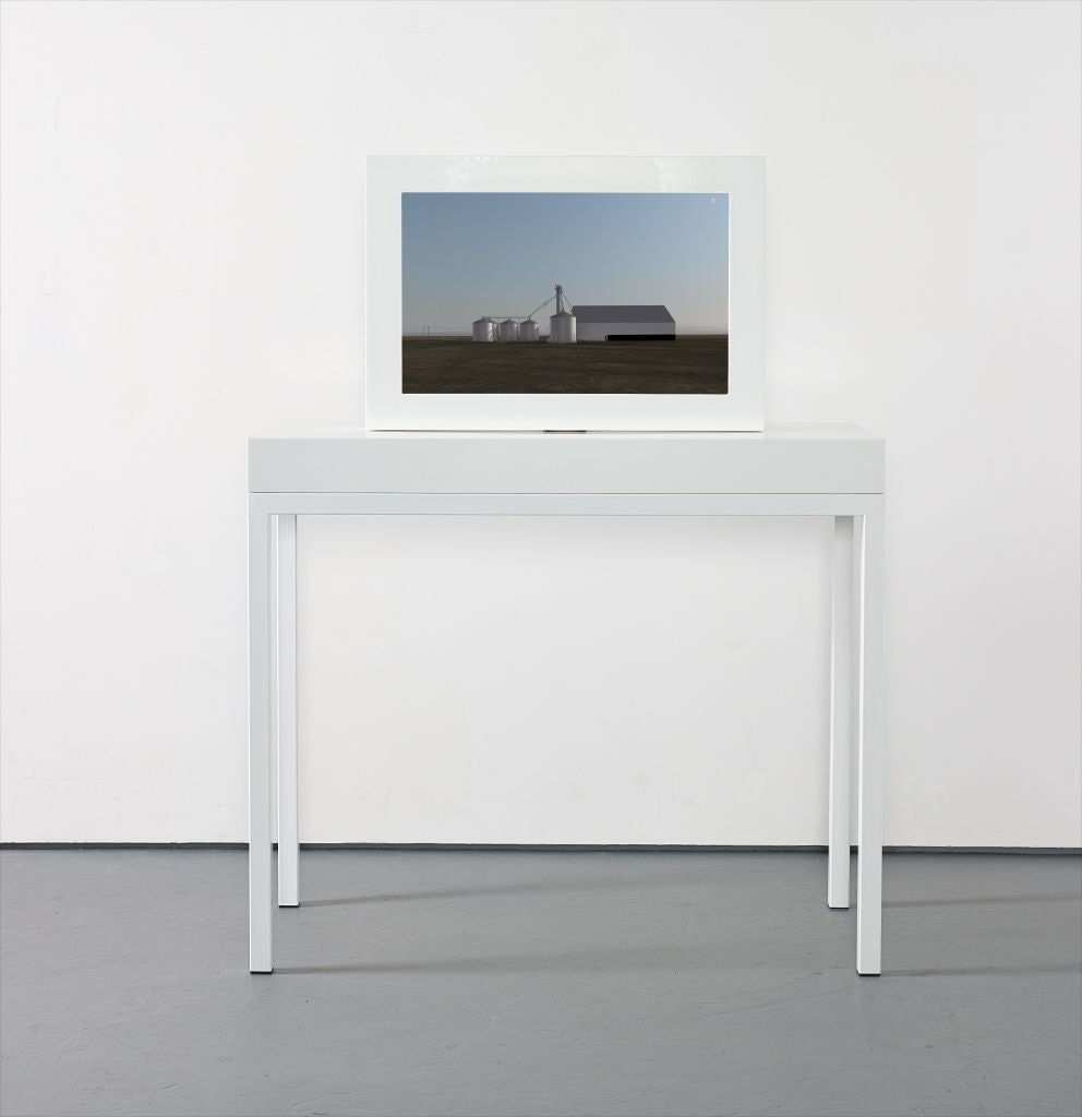 A white framed screen on a white table showing grain silos and a white barn on a flat field