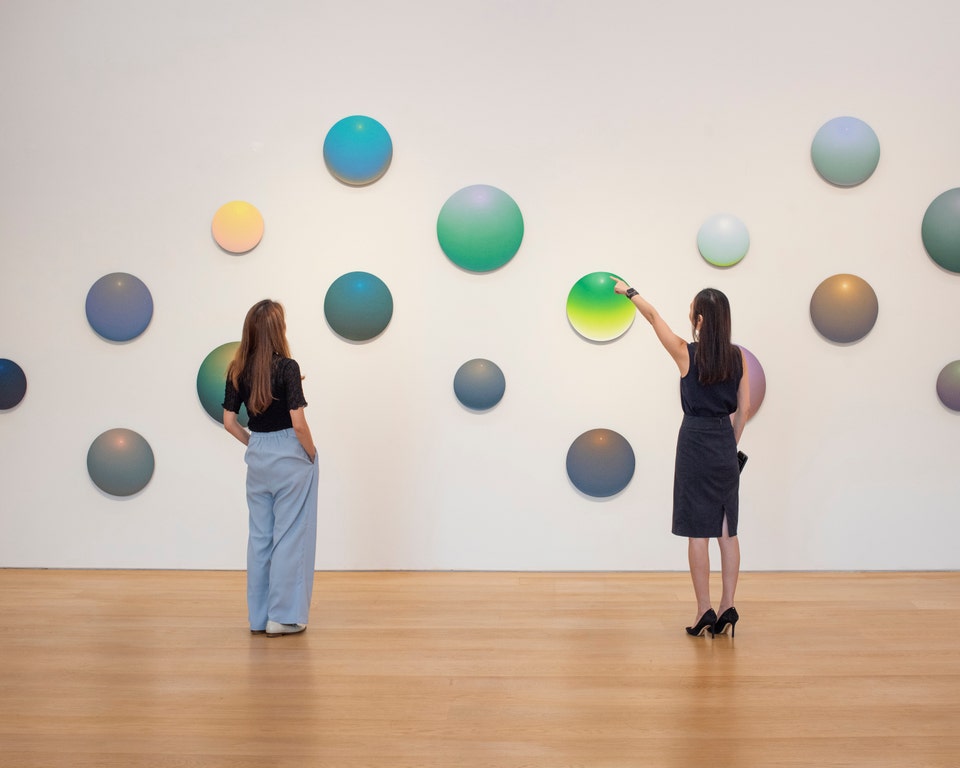 Two visitors viewing a colorful sculptural artwork in a gallery